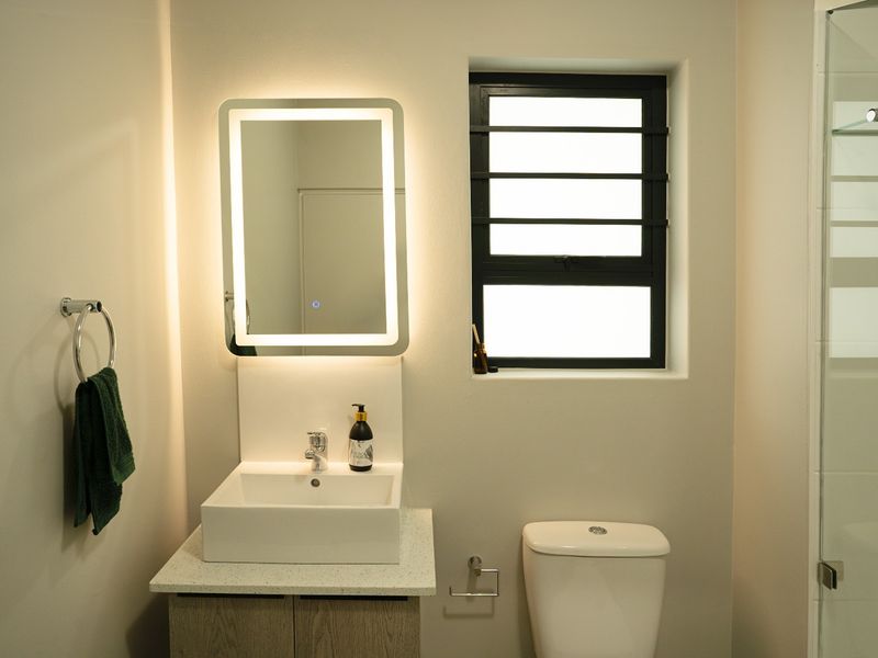 Modern bathroom featuring a vessel sink vanity, LED backlit mirror, toilet, and a glass-enclosed shower with contemporary finishes.