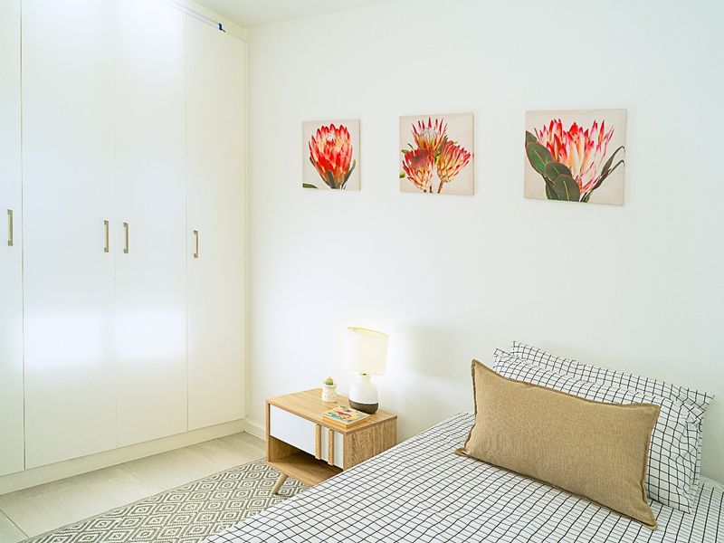 A bright and well-maintained bedroom featuring clean white walls and ample built-in cupboard storage.