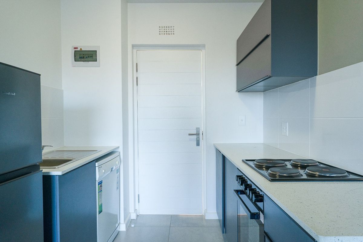 Modern galley-style kitchen featuring dark cabinetry, stone countertops, integrated electric hob and oven, and tiled flooring.