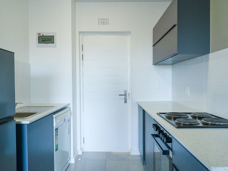 Modern galley-style kitchen featuring dark cabinetry, stone countertops, integrated electric hob and oven, and tiled flooring.