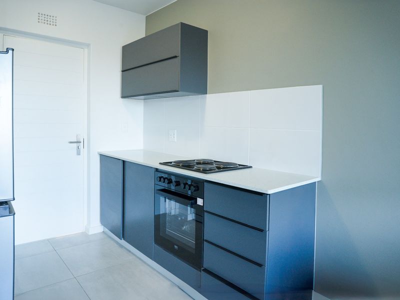 Modern kitchen featuring dark grey cabinetry, stone countertops, built-in oven, electric hob, and white tiled splashback in a clean, minimalist space.