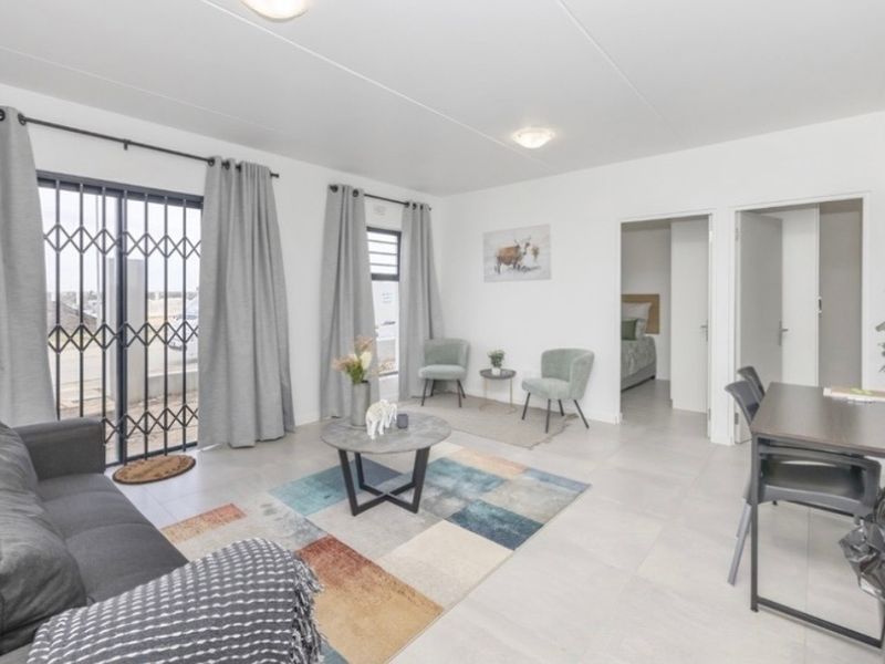 Bright open-plan living area featuring neutral tiled flooring, large sliding doors with security gates, and direct access to adjacent rooms.