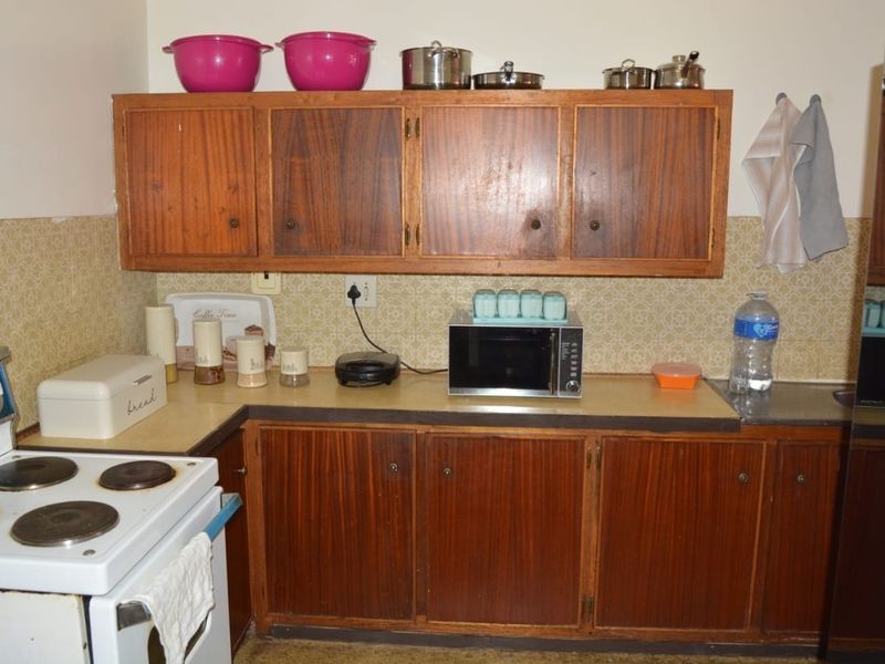 A dated kitchen featuring original wooden cabinetry, laminate countertops, and a classic electric stove, offering significant potential for a modern renovation.