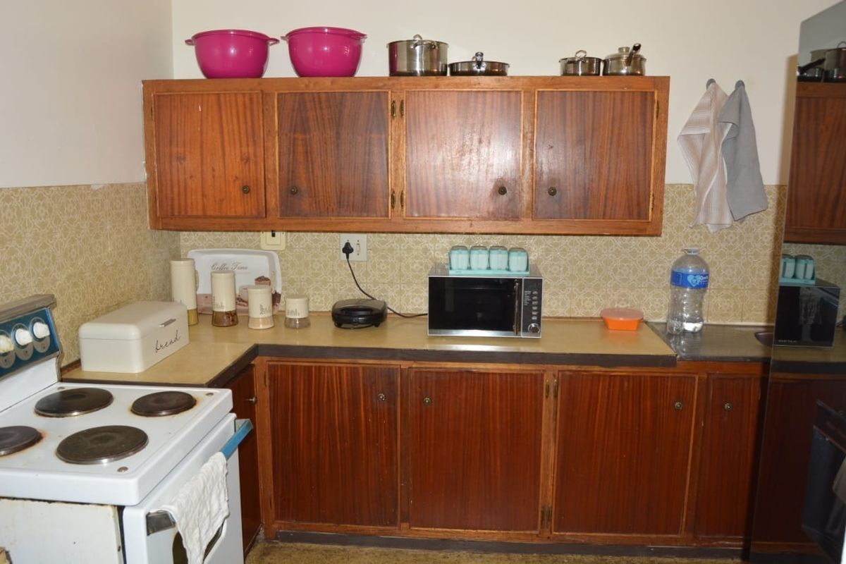 A dated kitchen featuring original wooden cabinetry, laminate countertops, and a classic electric stove, offering significant potential for a modern renovation.