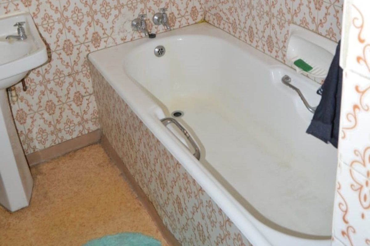 A dated bathroom featuring a standard bathtub with chrome fixtures and a pedestal basin, finished with patterned wall tiles.