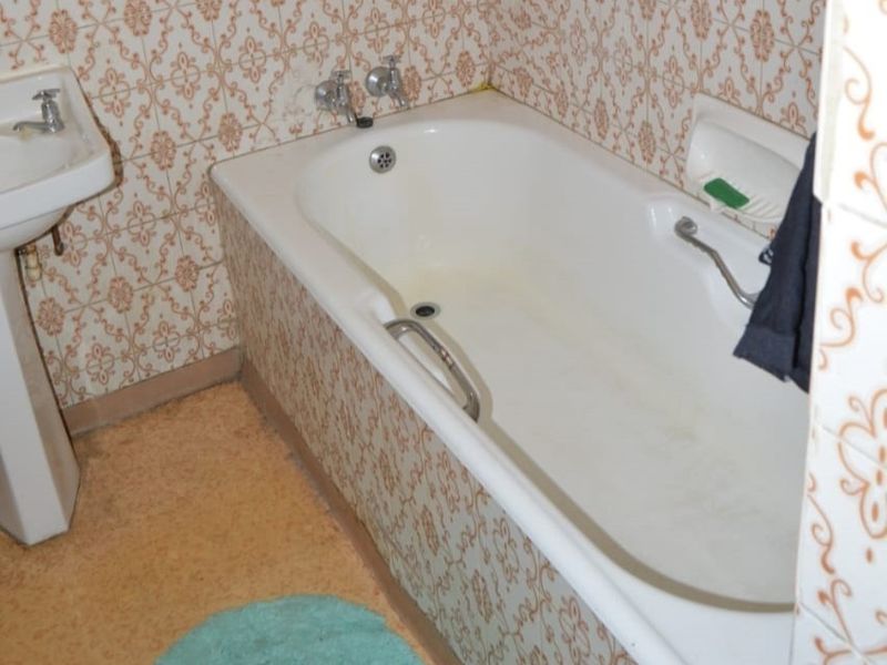 A dated bathroom featuring a standard bathtub with chrome fixtures and a pedestal basin, finished with patterned wall tiles.