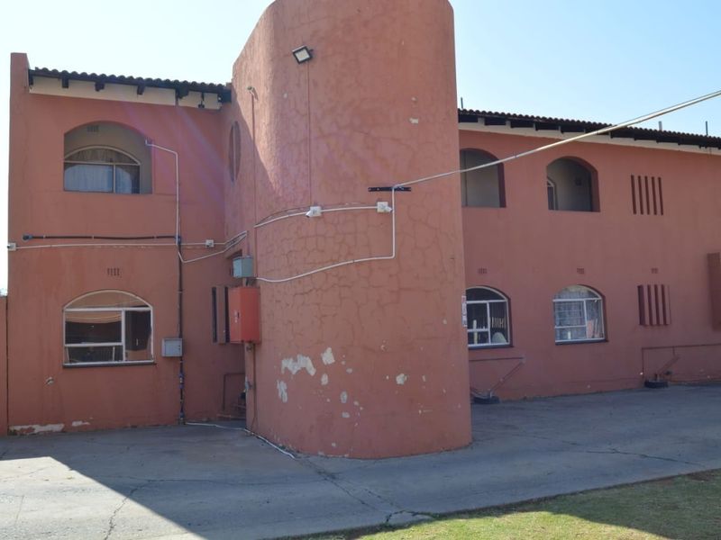 Front exterior view of a multi-story apartment building featuring arched windows, security bars, and a concrete driveway area.