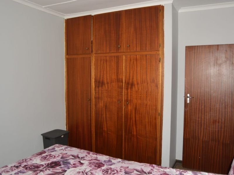 A bedroom featuring a large, dated built-in wooden wardrobe and a matching wooden door, providing ample storage space.
