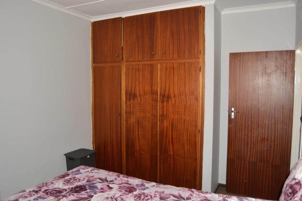 A bedroom featuring a large, dated built-in wooden wardrobe and a matching wooden door, providing ample storage space.