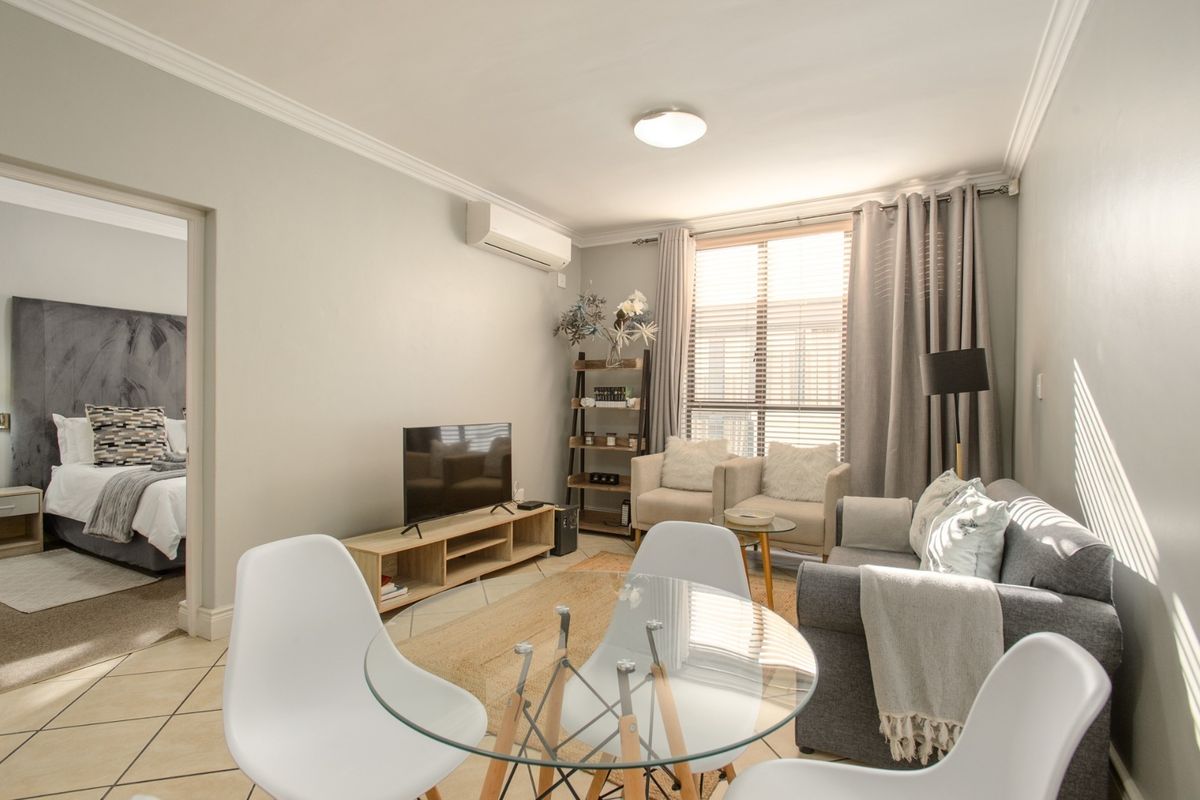 Open-plan living area featuring tiled flooring, crown molding, and a wall-mounted air conditioning unit, with an adjacent bedroom visible.