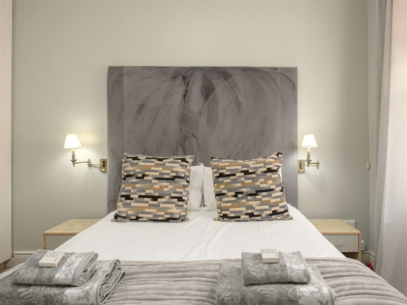 A well-maintained bedroom featuring a large upholstered headboard, integrated wall-mounted reading lights, and built-in wardrobe storage.