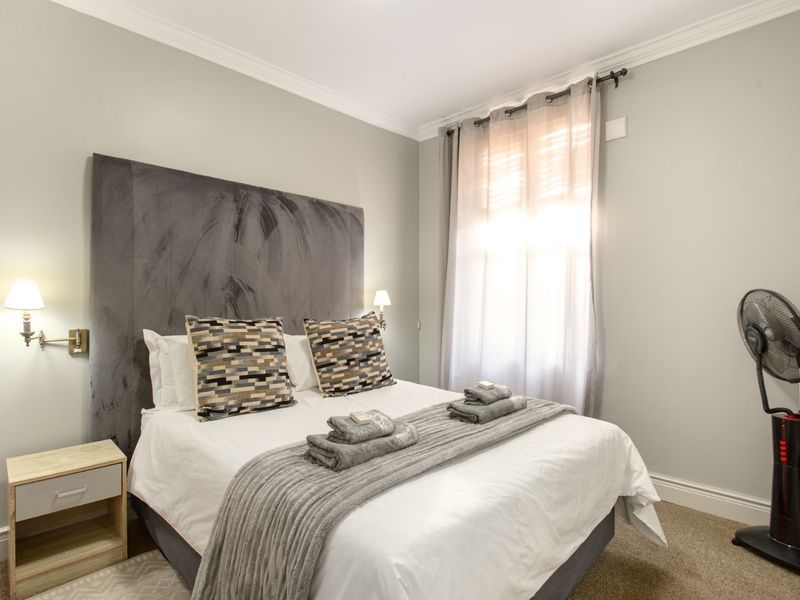 A well-maintained bedroom featuring neutral wall tones, carpeted flooring, crown molding, and wall-mounted bedside lighting.