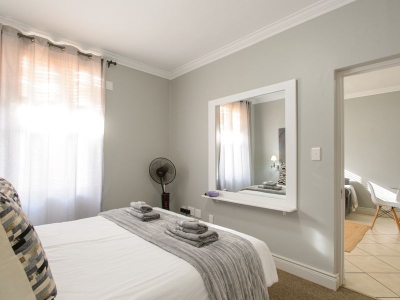 A well-maintained bedroom featuring neutral wall tones, crown molding, and a built-in wall mirror, with direct access to an adjacent tiled living area.