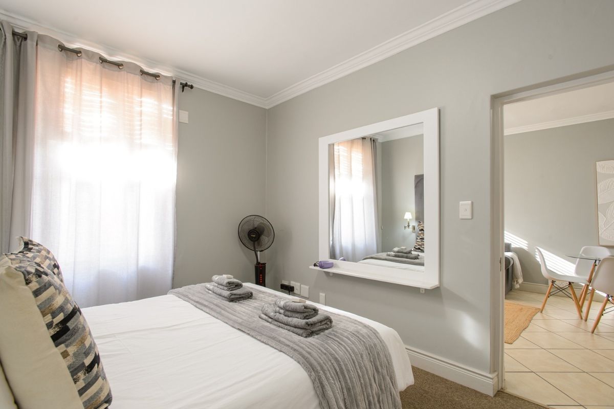 A well-maintained bedroom featuring neutral wall tones, crown molding, and a built-in wall mirror, with direct access to an adjacent tiled living area.
