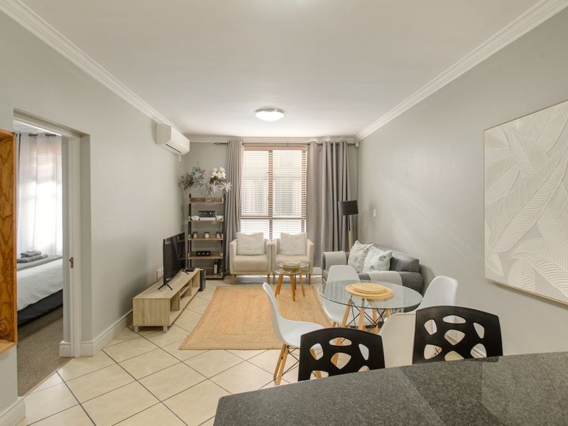 A well-maintained open-plan living and dining area featuring tiled floors, crown molding, and a split-system air conditioner.