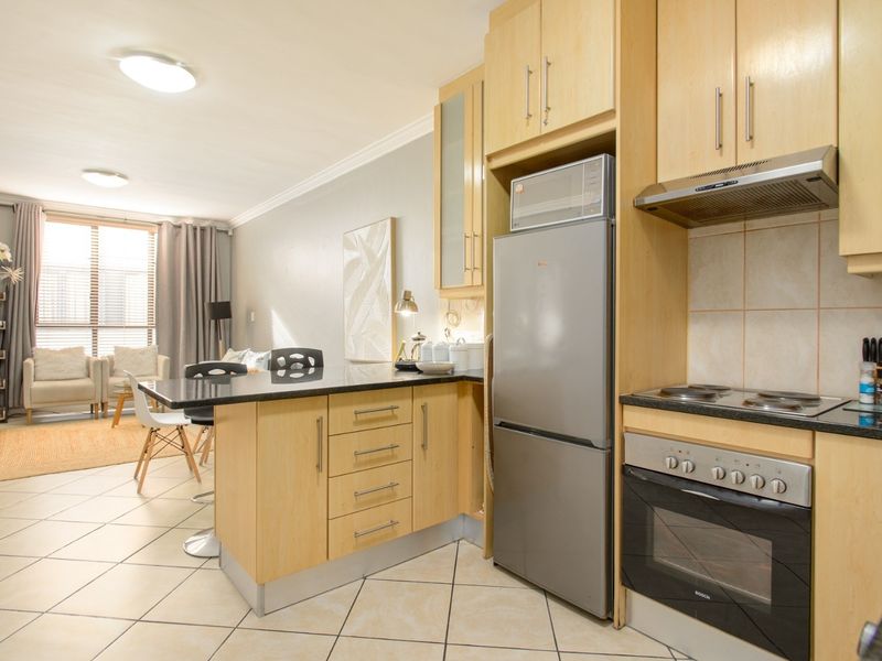 Open-plan kitchen and living area featuring light wood cabinetry, granite countertops, integrated appliances, and tiled flooring throughout.