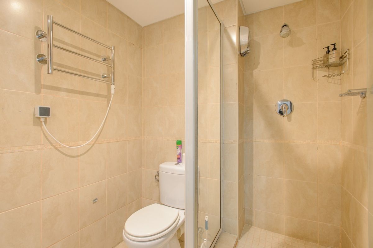 A compact bathroom featuring a glass-enclosed shower, a standard toilet, and a wall-mounted heated towel rail with neutral wall tiling.