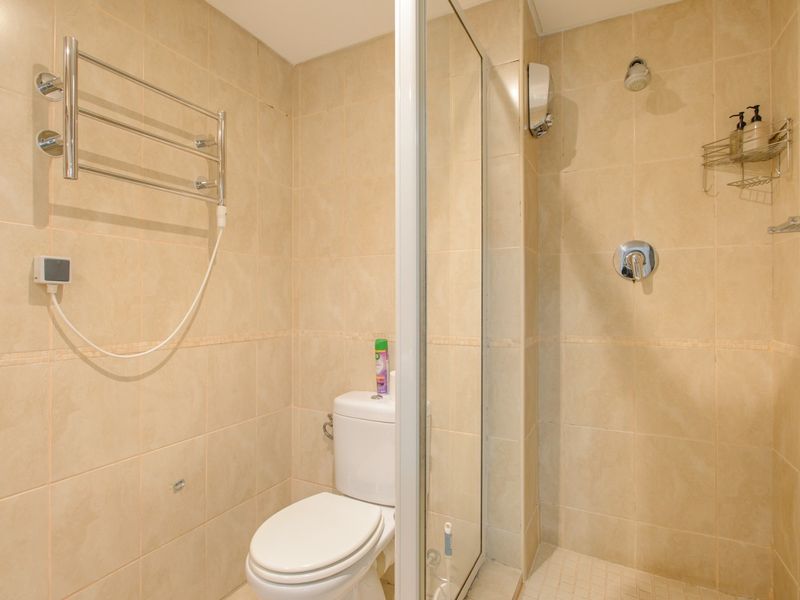 A compact bathroom featuring a glass-enclosed shower, a standard toilet, and a wall-mounted heated towel rail with neutral wall tiling.