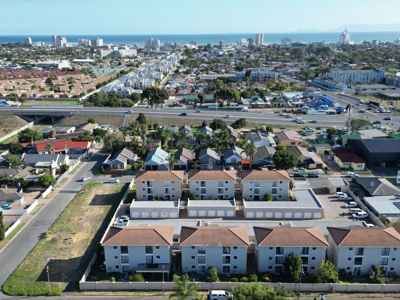 An aerial view of the apartment complex showing the building layout, tiled roofs, garage units, and surrounding neighborhood infrastructure.
