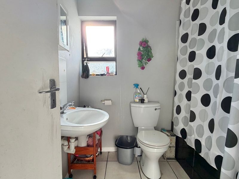 A compact bathroom featuring a pedestal basin, toilet, and shower area with tiled flooring and a window for natural light.