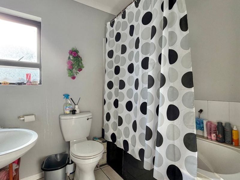 A functional bathroom featuring a pedestal basin, toilet, and a bathtub with a shower curtain rail, requiring minor cosmetic updates.