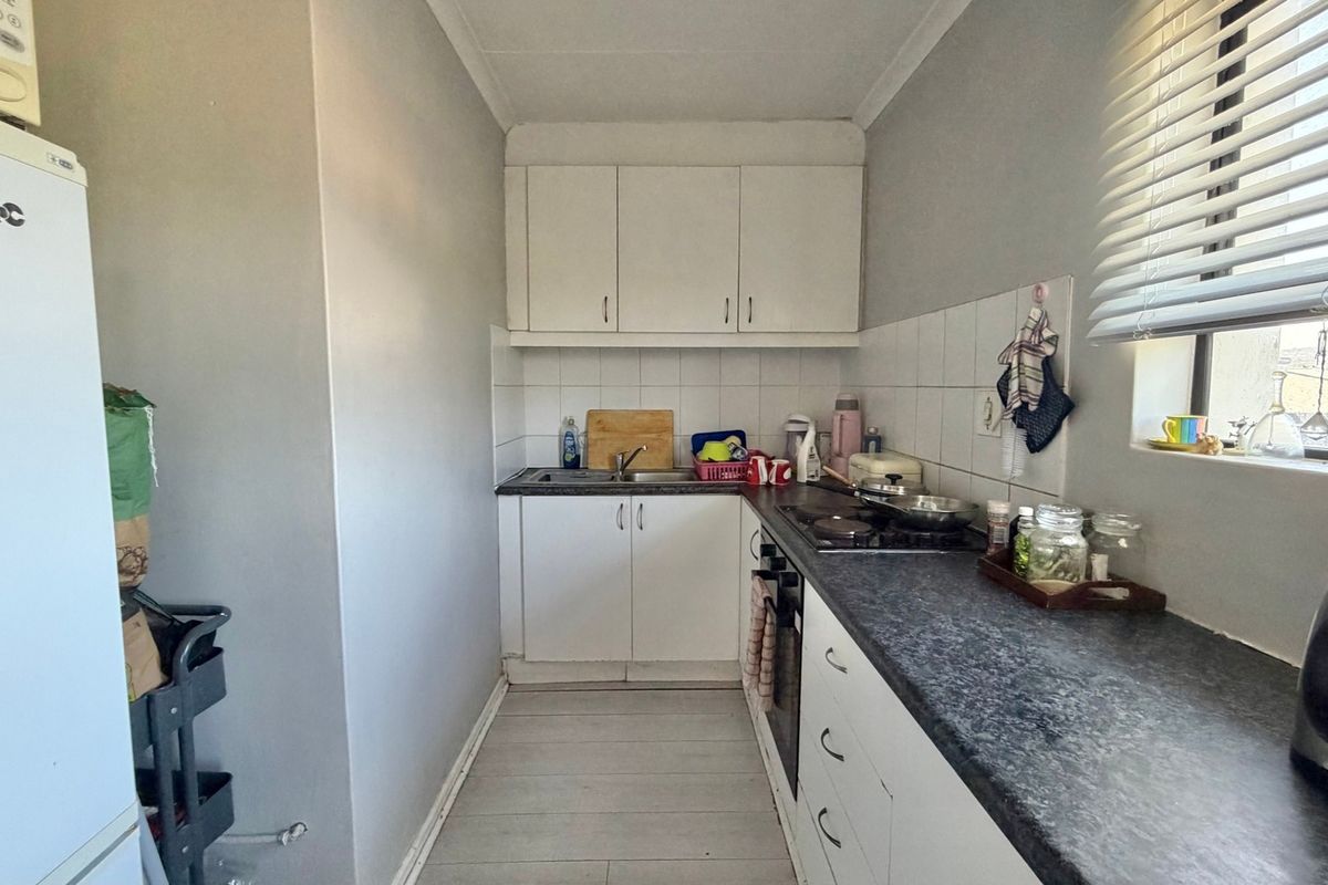 A compact galley-style kitchen featuring white cabinetry, dark laminate countertops, a built-in oven, and a tiled backsplash with a window for natural light.