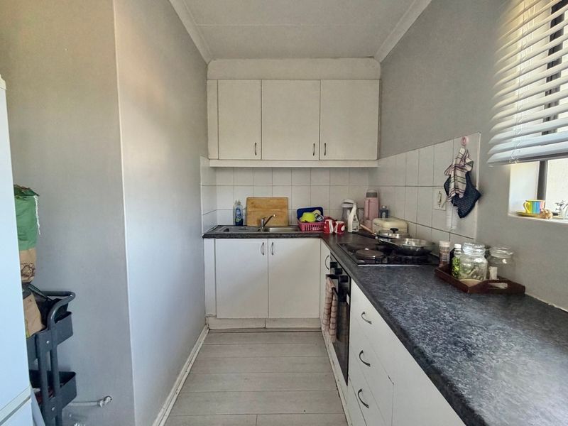 A compact galley-style kitchen featuring white cabinetry, dark laminate countertops, a built-in oven, and a tiled backsplash with a window for natural light.