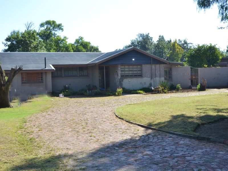 Front view of a single-story house featuring a brick driveway, tiled roof, and established garden area.