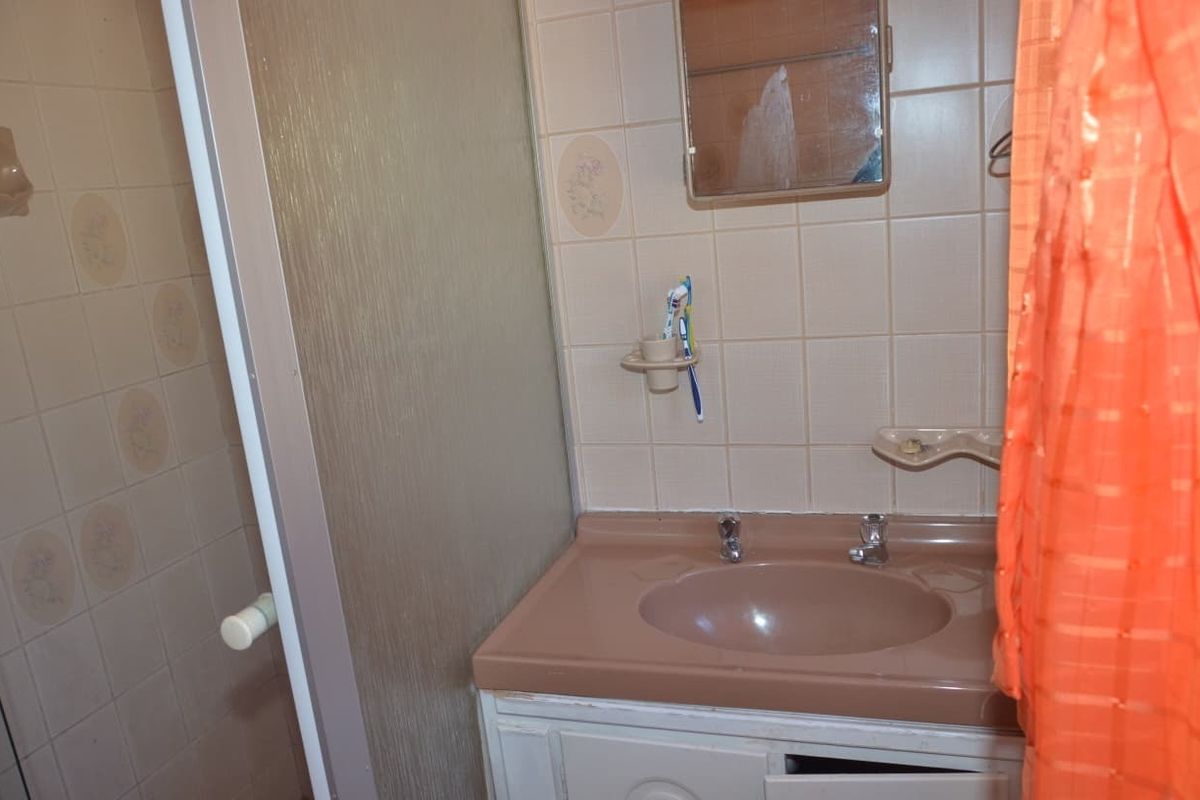 A dated bathroom featuring a vanity unit with an integrated basin, shower enclosure, and wall tiling, requiring modernization to improve functionality and aesthetic appeal.