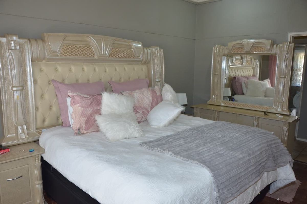 A bedroom featuring a large bed with a decorative headboard and a matching built-in mirror unit.