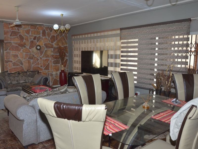 Open plan living and dining area featuring a prominent stone accent wall, tiled flooring, and large windows with fitted blinds.