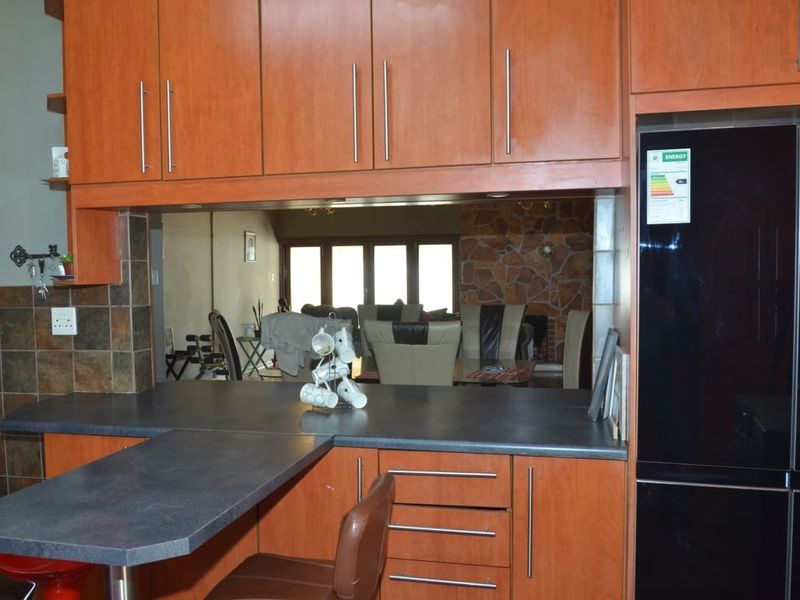 A functional kitchen featuring wood-look cabinetry, dark laminate countertops, and a breakfast bar, with a pass-through window overlooking the adjacent living area.