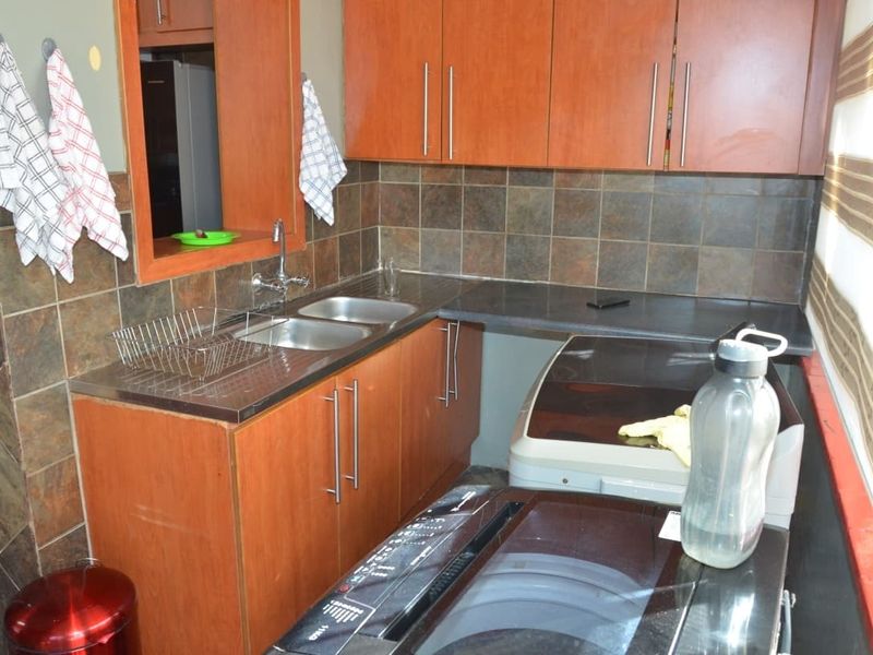 A functional laundry area featuring wood-look cabinetry, a double stainless steel sink, and tiled splashbacks, providing practical utility space.