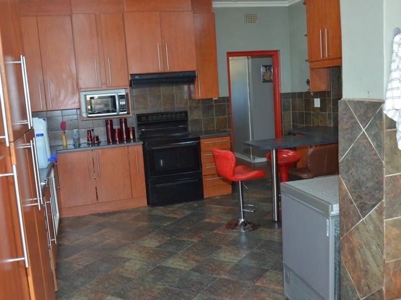 A functional kitchen featuring wood-tone cabinetry, dark tiled backsplash, integrated appliances, and a breakfast bar area with tiled flooring throughout.