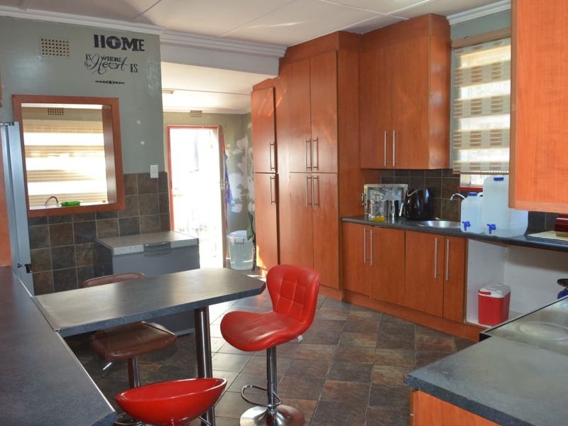 A functional kitchen featuring wooden cabinetry, tiled flooring, and a tiled backsplash, currently showing signs of wear and requiring cosmetic updates.