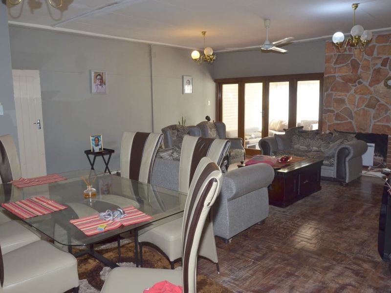 Spacious open-plan living and dining area featuring a prominent stone fireplace, ceiling fan, and direct access to the patio through sliding glass doors.