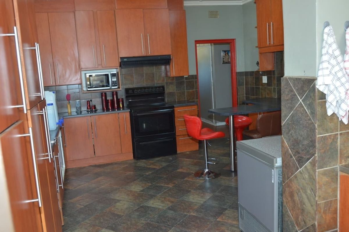 A functional kitchen featuring wood-tone cabinetry, dark tiled backsplash, integrated appliances, and a breakfast bar area with tiled flooring throughout.
