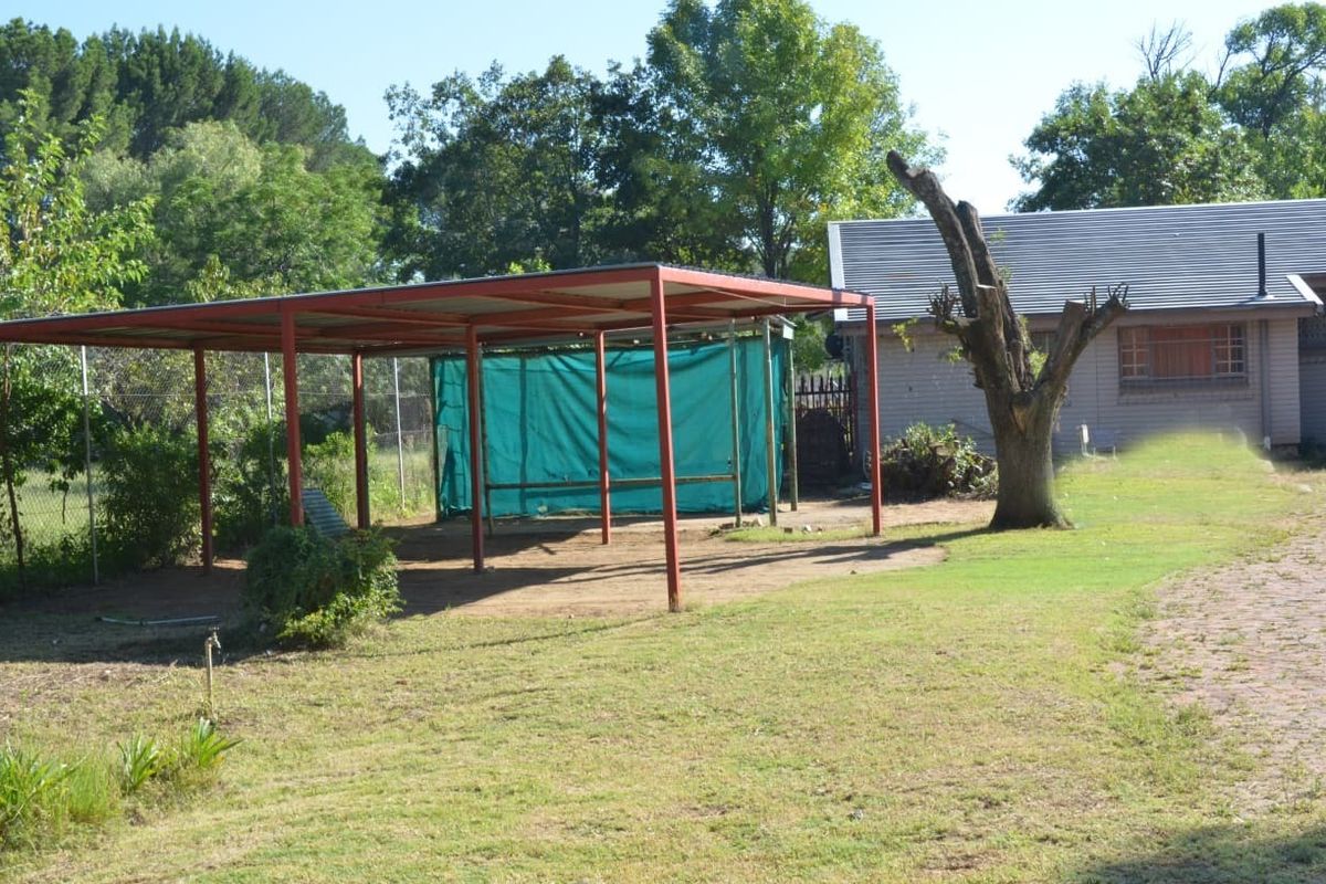 Rear garden area featuring a metal carport structure with shade cloth screening and a large lawn area.