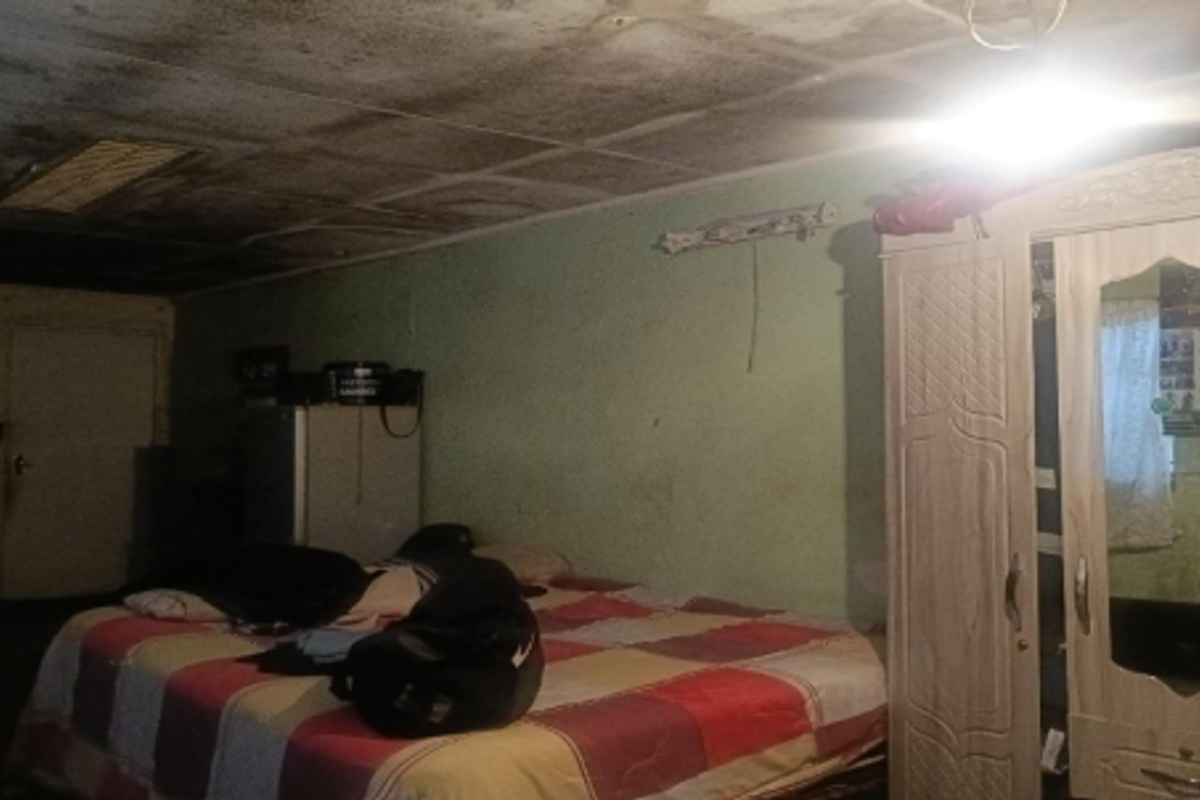 A bedroom featuring a damaged ceiling with significant water staining and peeling paint, requiring immediate repair and renovation.