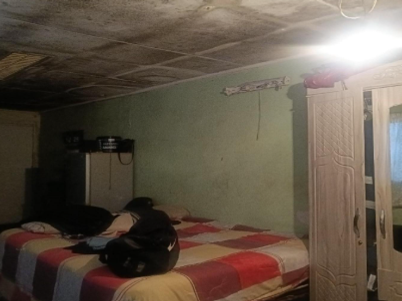 A bedroom featuring a damaged ceiling with significant water staining and peeling paint, requiring immediate repair and renovation.