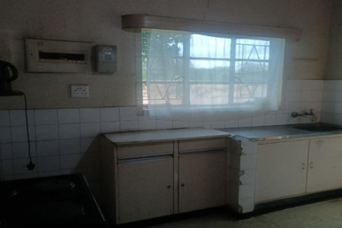 A dated kitchen featuring basic cabinetry, a stainless steel sink, and tiled splashbacks, requiring modernization and repair of fixed finishes.