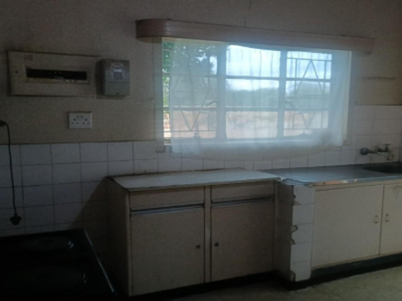 A dated kitchen featuring basic cabinetry, a stainless steel sink, and tiled splashbacks, requiring modernization and repair of fixed finishes.