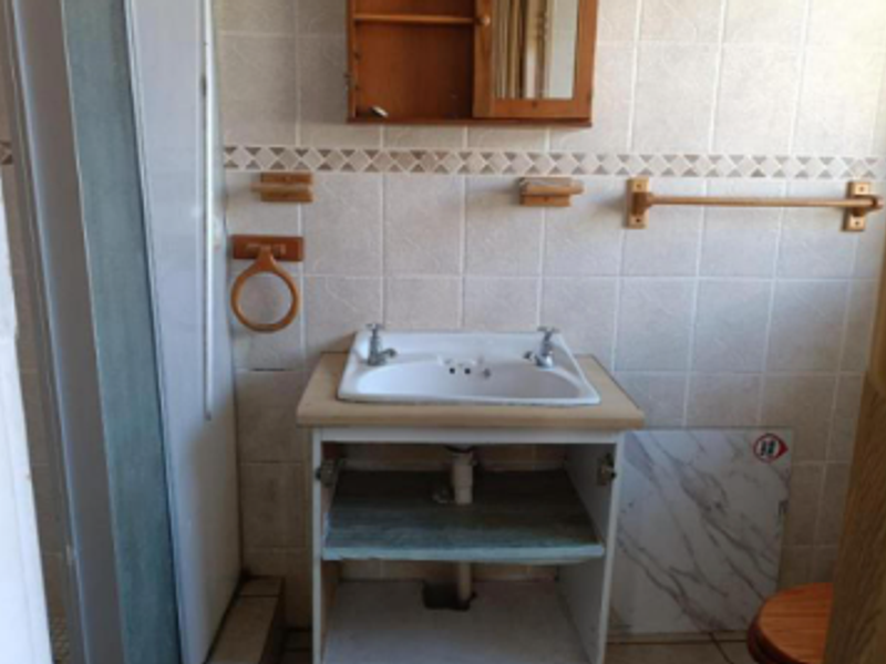 A dated bathroom featuring a vanity basin, shower enclosure, and wall tiling, currently requiring maintenance and cosmetic updates to the vanity and flooring.
