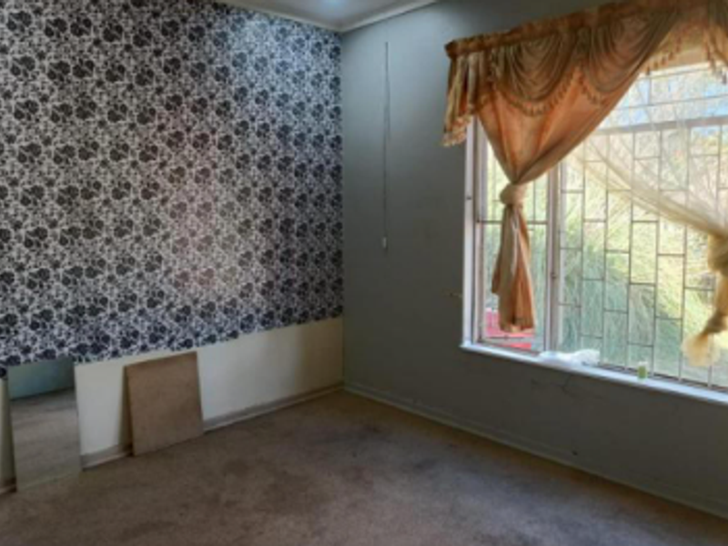 An empty bedroom featuring patterned wallpaper, carpet flooring, and a window fitted with security bars.
