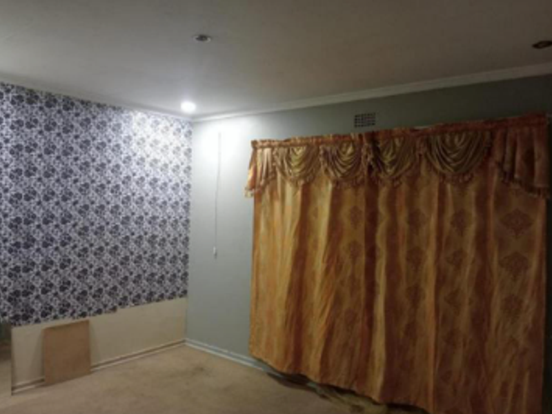 An empty bedroom featuring recessed downlights, coving, and a combination of patterned wallpaper and painted walls.