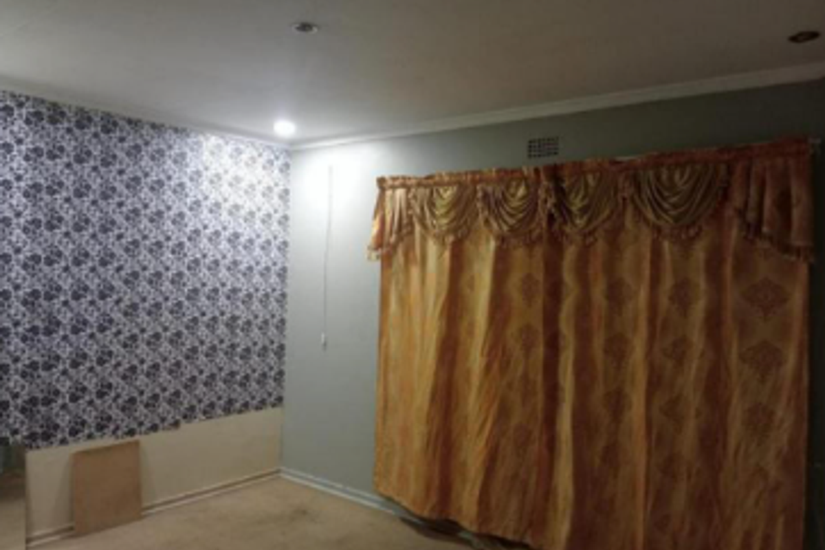 An empty bedroom featuring recessed downlights, coving, and a combination of patterned wallpaper and painted walls.