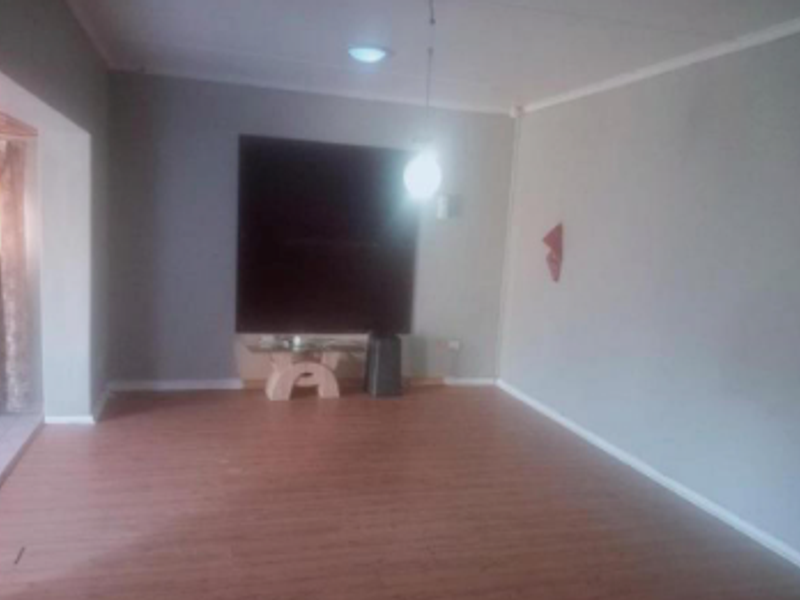 A spacious, empty living room featuring laminate flooring, neutral grey walls, and simple pendant lighting, offering a blank canvas for interior design.
