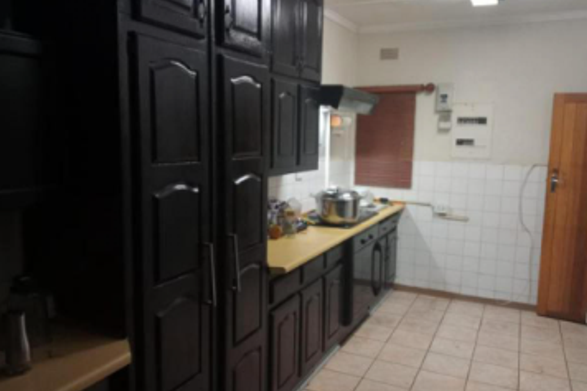 A functional kitchen featuring dark built-in cabinetry, tiled splashbacks, and tiled flooring, offering a dated aesthetic with potential for modernization.