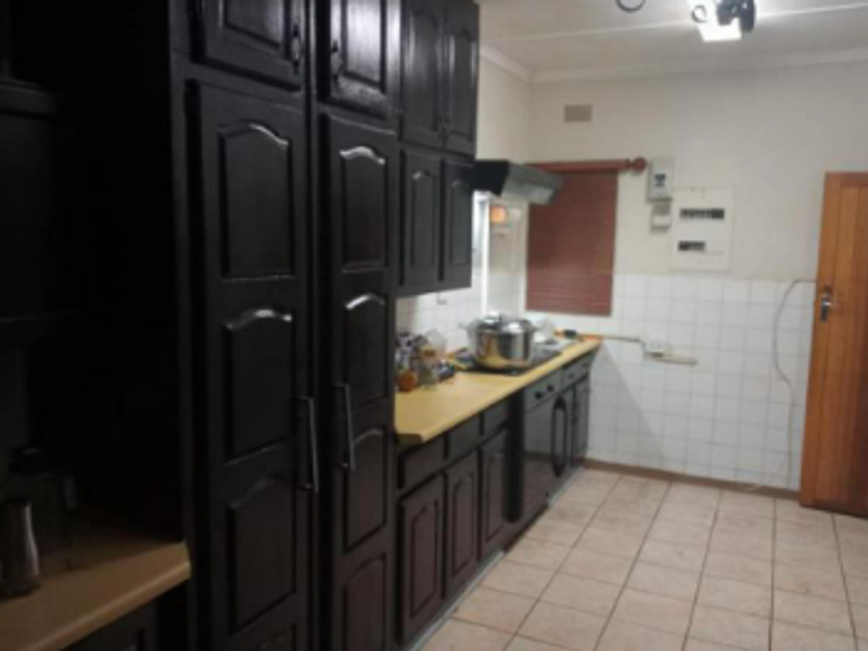 A functional kitchen featuring dark built-in cabinetry, tiled splashbacks, and tiled flooring, offering a dated aesthetic with potential for modernization.