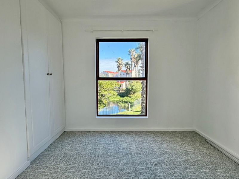 A bright, empty bedroom featuring built-in cupboards, carpeted flooring, and a window with a pleasant outdoor view.
